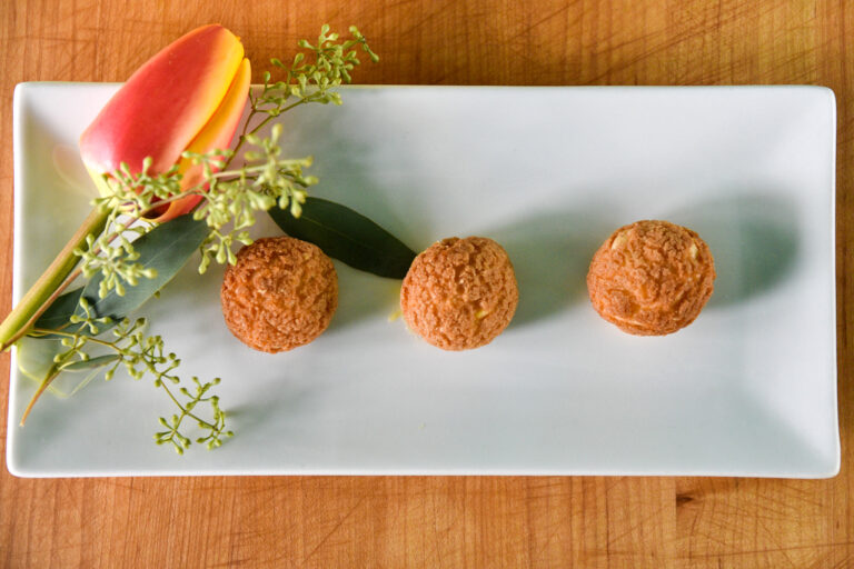 Grapefruit Pate a Choux (sphere shaped pastries) plated on a rectangular white plate with a tulip and greenery, made by Anna Szeto, AFICI