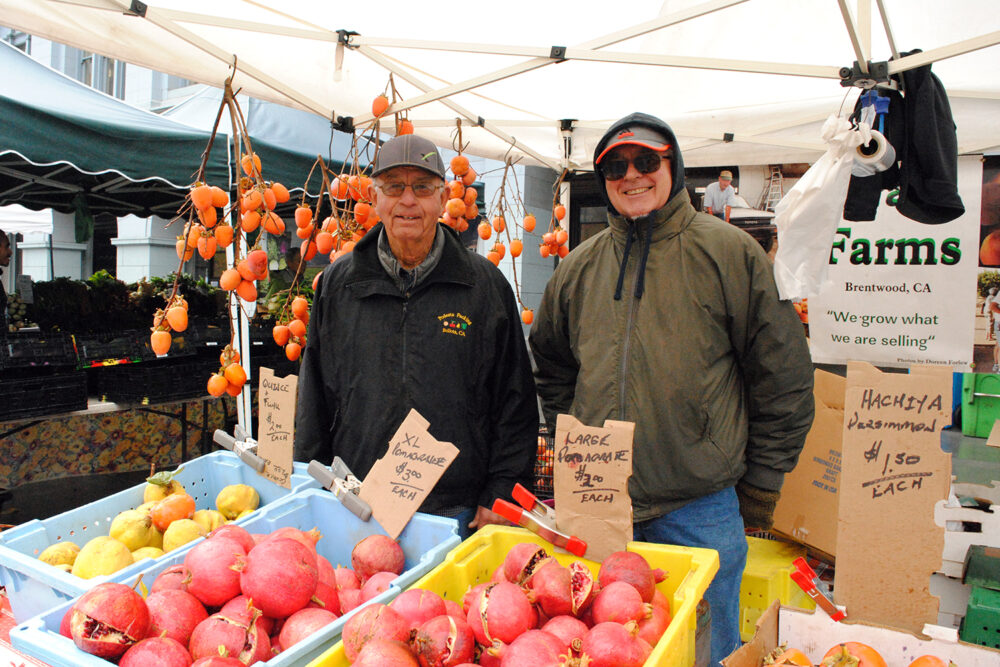 Two people, including Mike Arata, pose behind crates of pomegranates at Arata Farms' stand at Foodwise's Ferry Plaza Farmers Market in San Francisco.