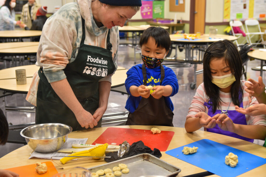 An adult and two kids cook together at a table