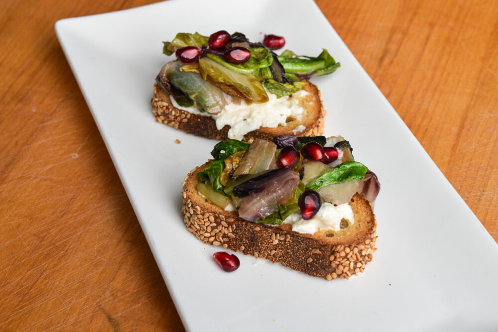 Bruschetta topped with braised chicories on a white plate.