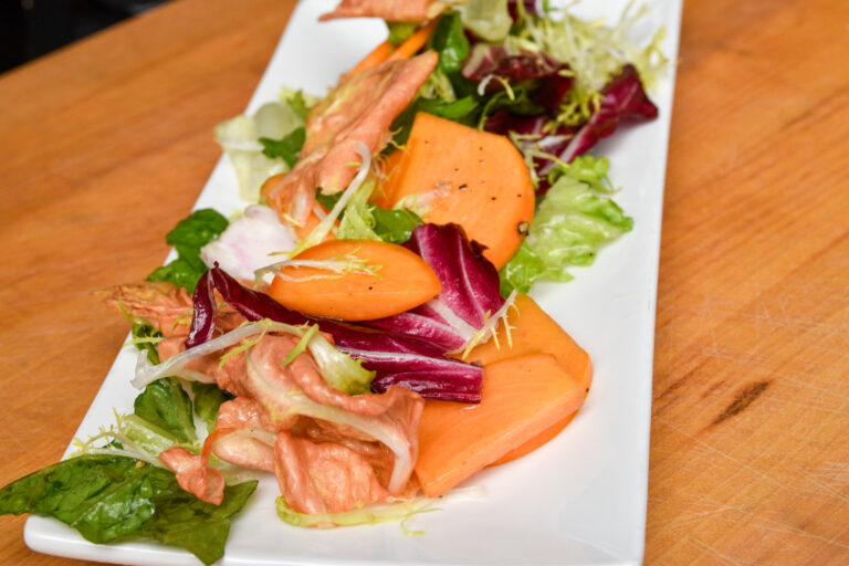 A chicory and persimmon salad on a white plate.