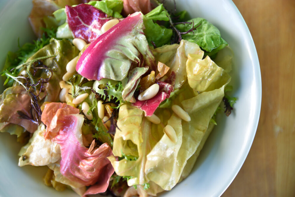 Bright green and pink chicories, topped with pine nuts, served in a white dish