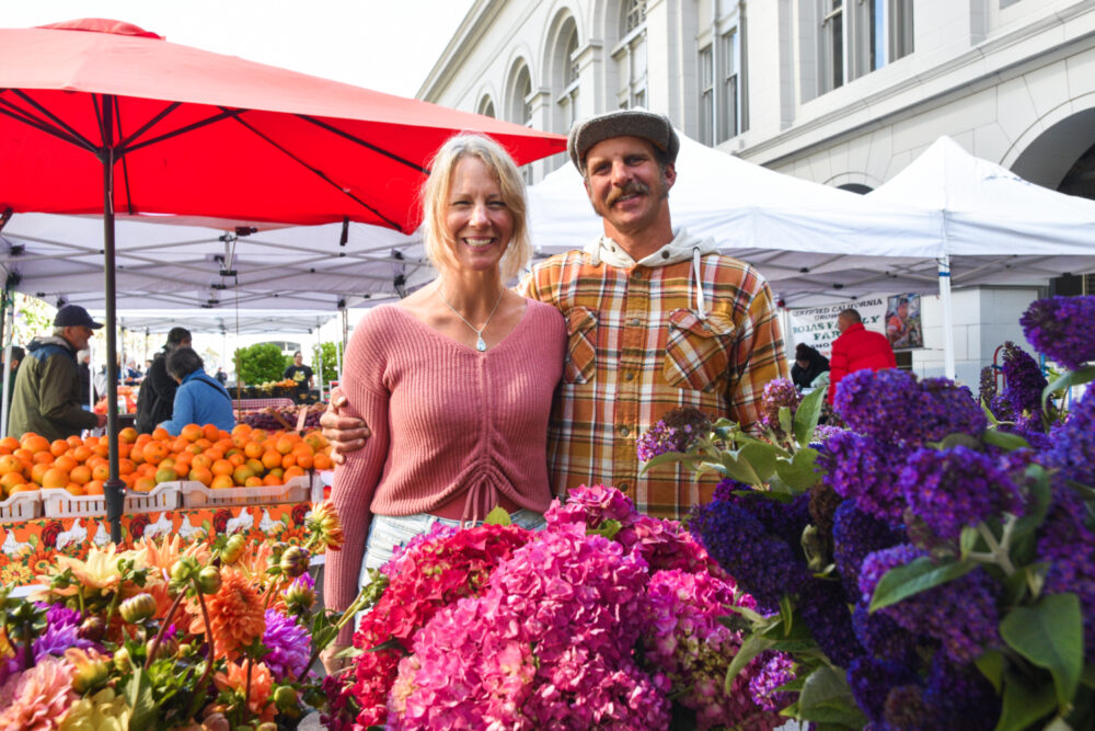 Farmers Molly and Ken stand behind pink and purple flowers