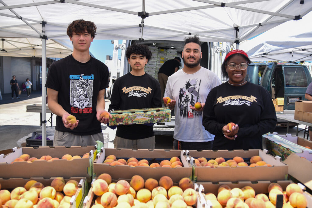 Foodwise Teens pose for  a photo at Frog Hollow Farm's stand at the Ferry Plaza Farmers Market. Peaches and stone fruit are in the foreground.