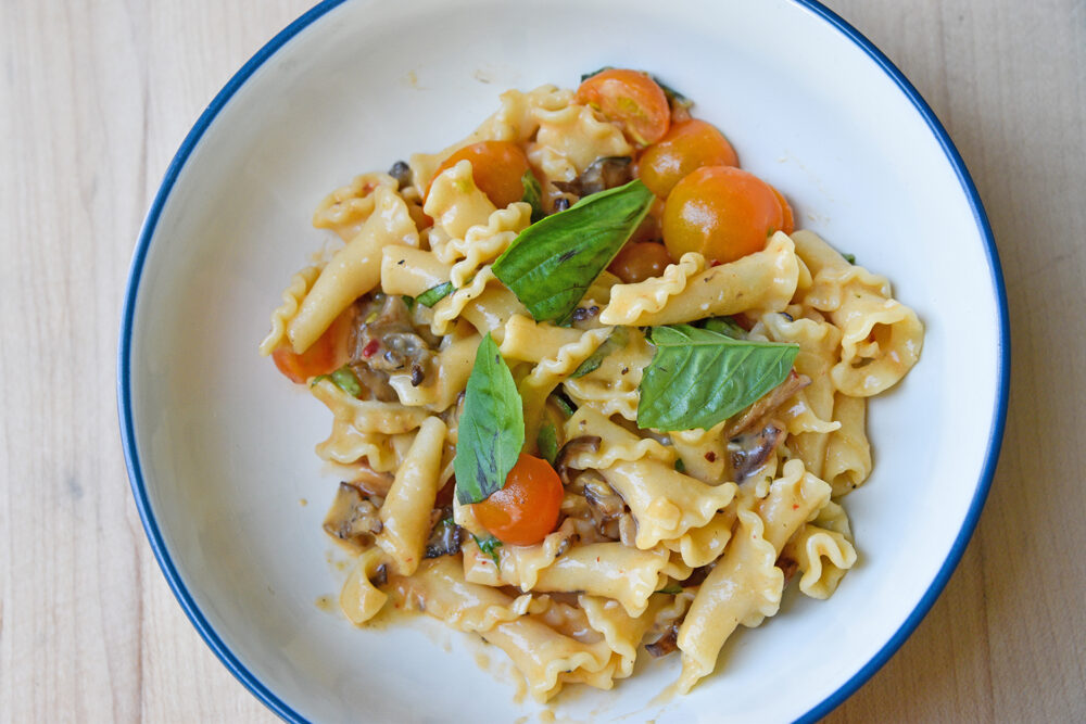 Bowl of pasta and vegetables, topped with basil