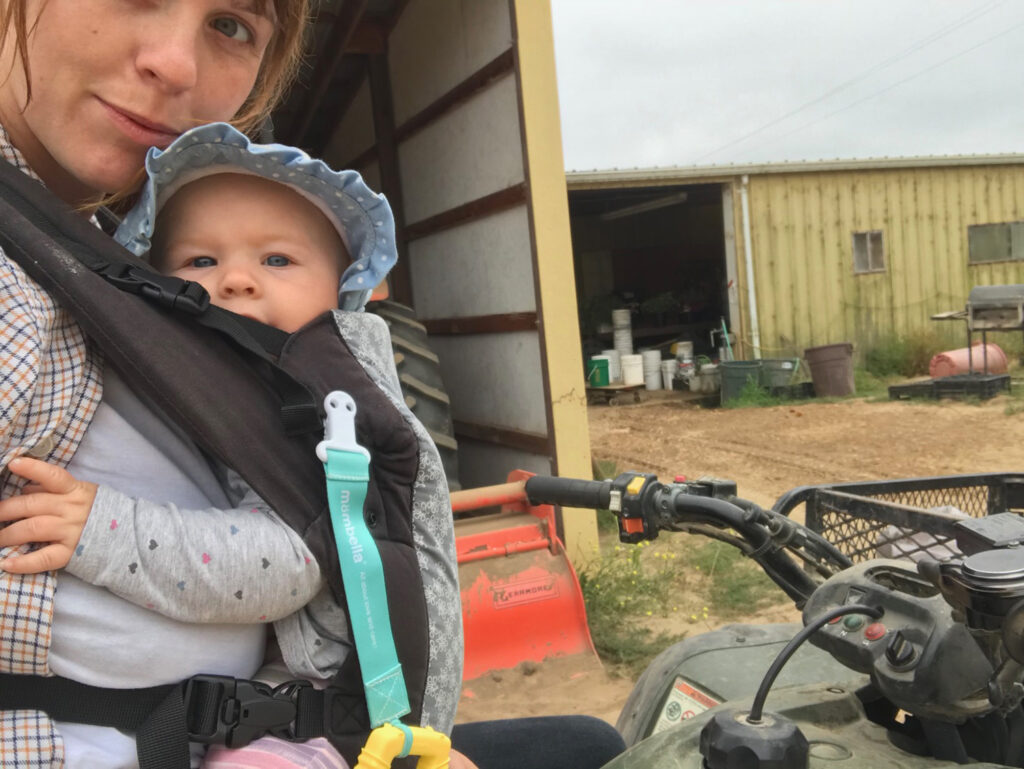 A selfie of a woman holding a baby on a farm.