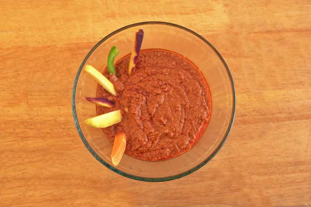 Maafe, also known as Peanut Stew, in a glass bowl on a wooden cutting board.