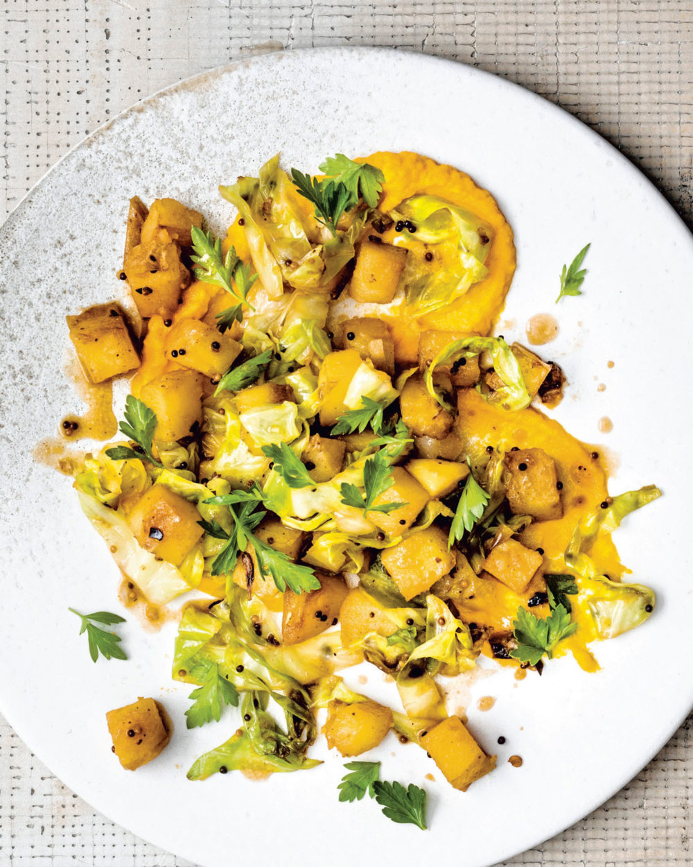 Sauteed cabbage topped with an orange carrot puree and green herbs, served on a white ceramic dish.